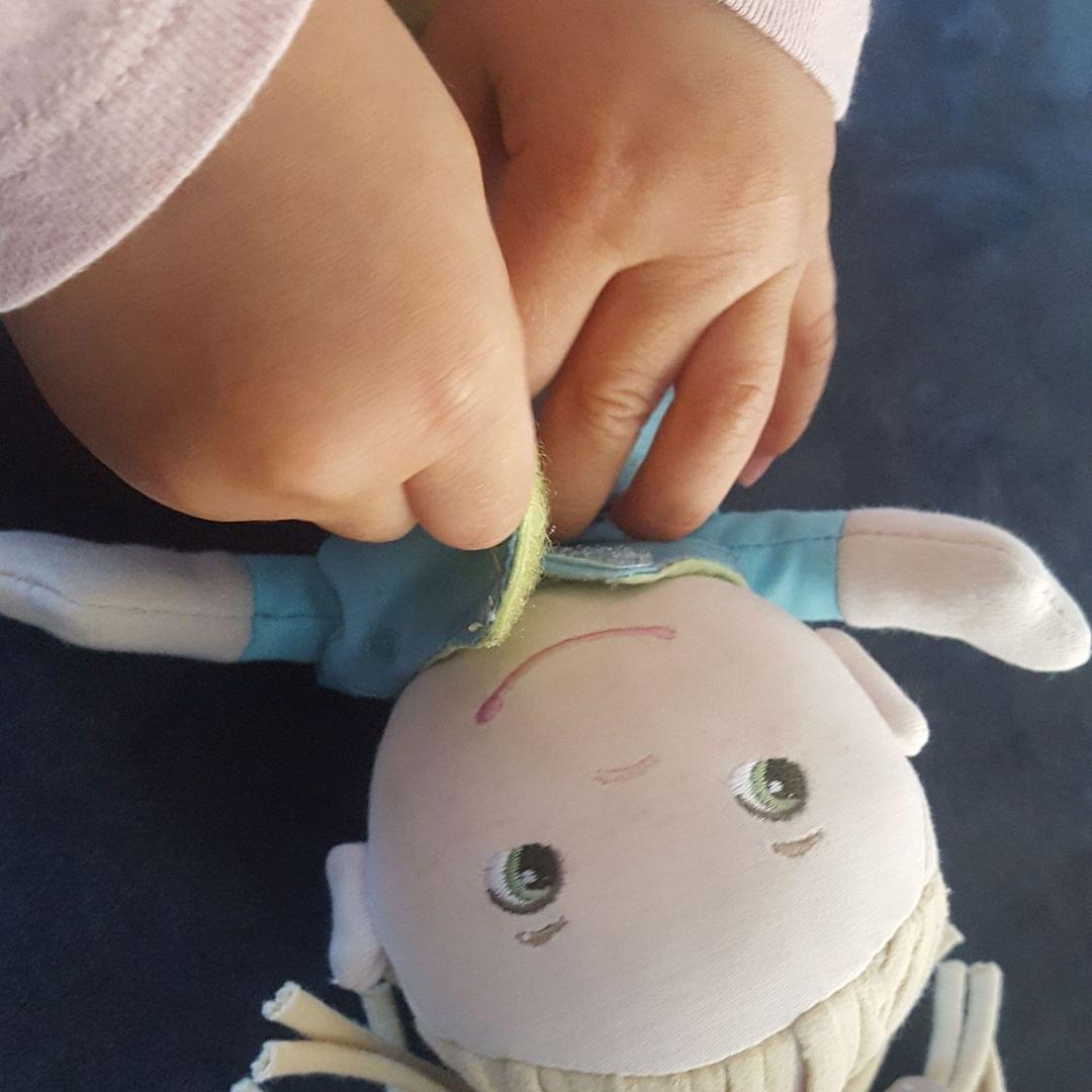 Foto von Kinderhänden, die eine Puppe anziehen