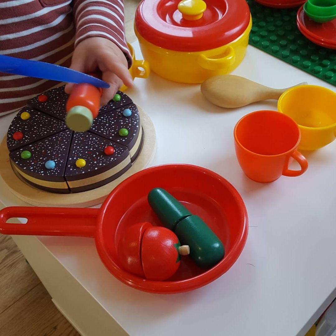 Foto eines Kindes, das mit Spielgeschirr auf einem Tisch spielt