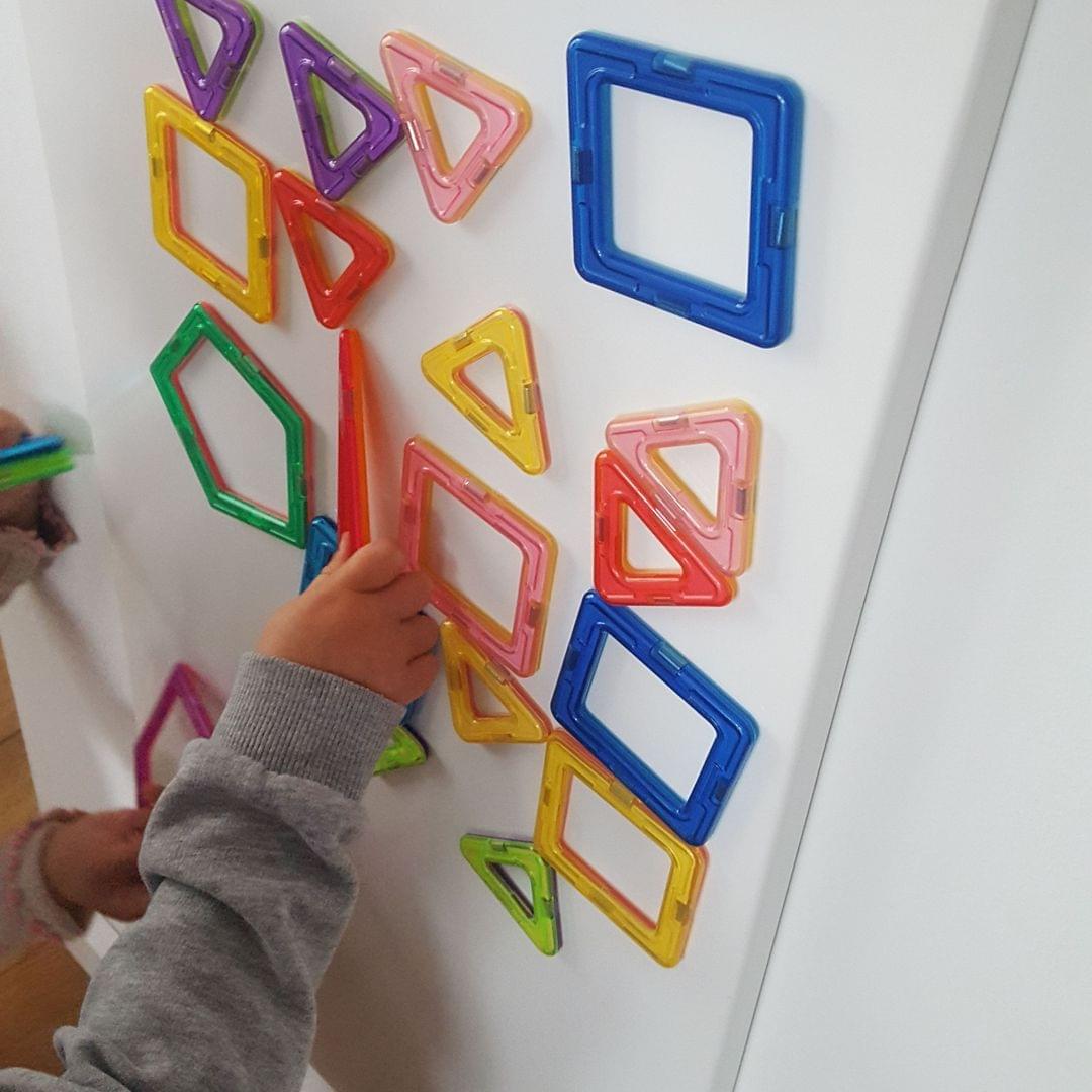 Foto eines Kindes, das an einer Magnetwand mit magnetischen, geometrischen Formen spielt