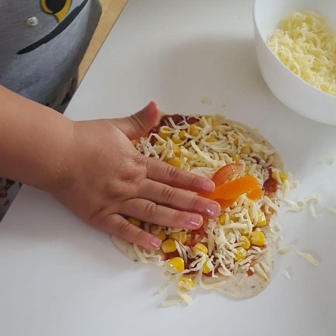 Foto einer Kinderhand, die eine Pizza belegt
